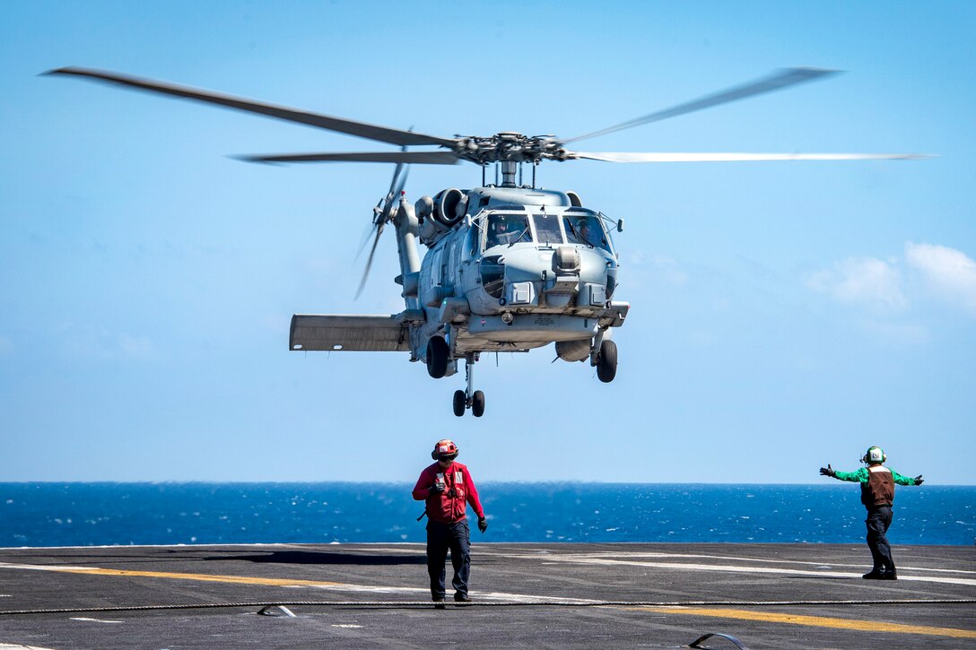 A Seahawk helicopter hovers over a flight deck after takeoff.