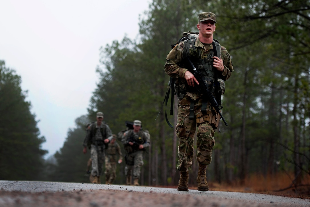 A soldier competes in a ruck march along a road..