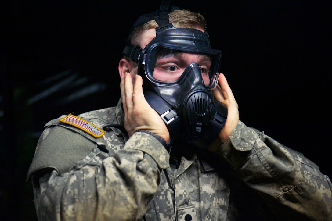 A soldier checks the seal of his gas mask.