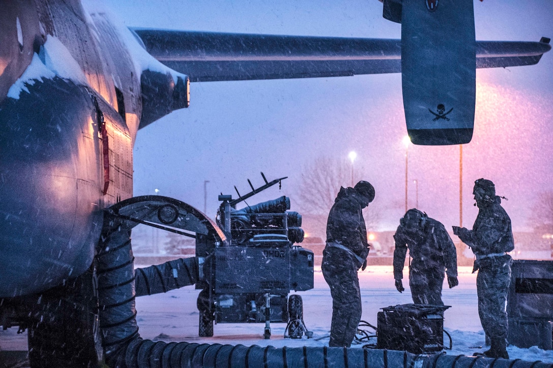 Airmen work on the brake systems of a Hercules aircraft during a snowstorm.