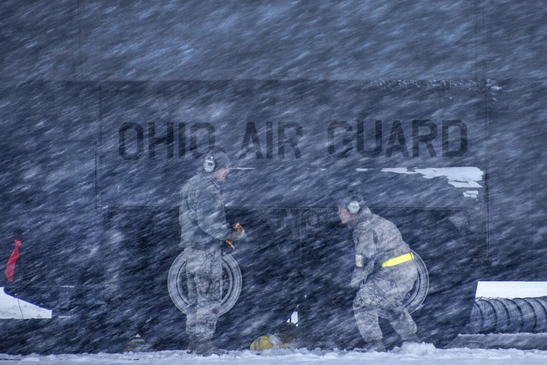 Airmen stand next to a Hercules aircraft during a snowstorm.