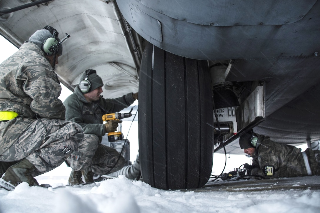 Airmen crouch next to a Hercules aircraft tire.