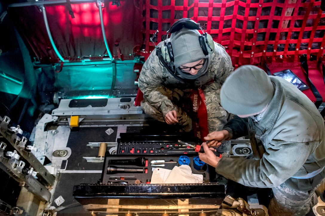 Two airmen look through a tool chest while inside a Hercules aircraft.