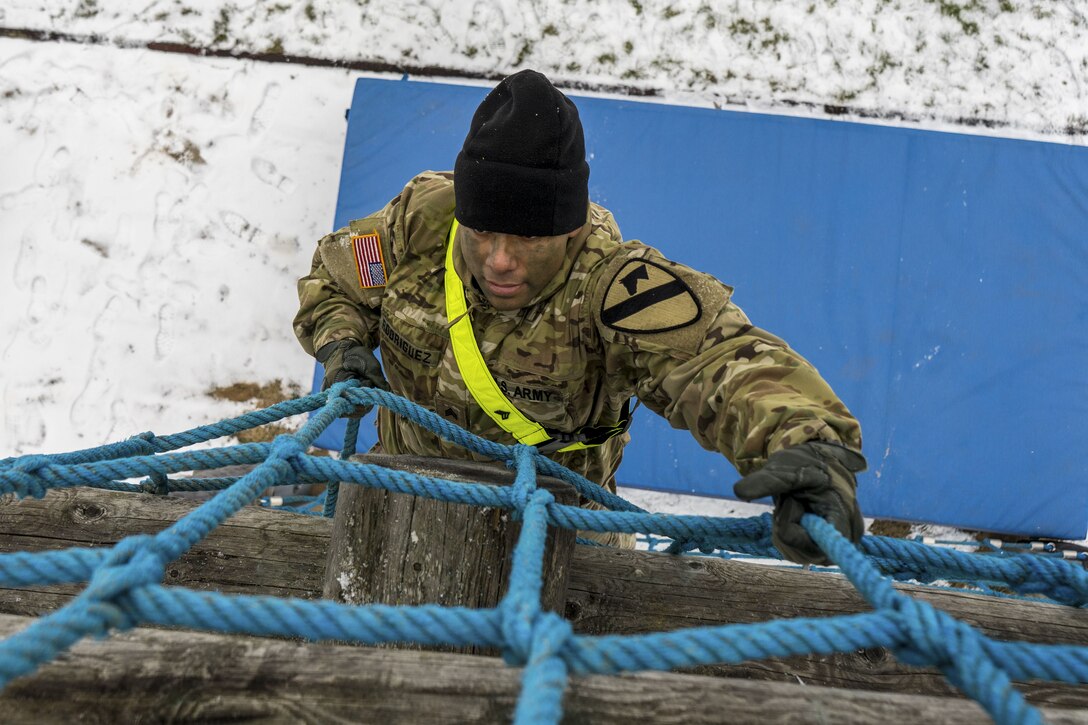 A soldiers climbs a 20-foot blue net.