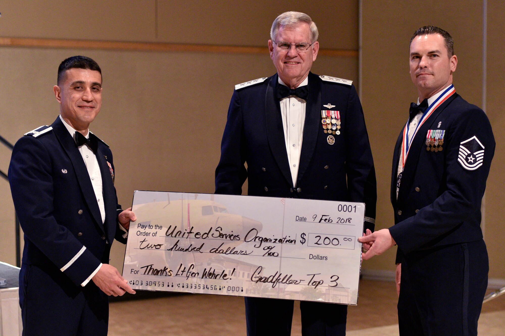 U.S. Air Force Col. Ricky Mills, 17th Training Wing commander, and Master Sgt. John Gregg, 17th Medical Operations Squadron superintendent, presents retired Lt. Gen. Joe Wherle with a $200 check to the United Services Organizations during the 25th Annual Awards Ceremony at the McNeese Convention Center in San Angelo, Texas, Feb. 9, 2018. The check was donated in Wherle’s name as a thank you for attending the ceremony. (U.S. Air Force photo by Senior Airman Randall Moose)