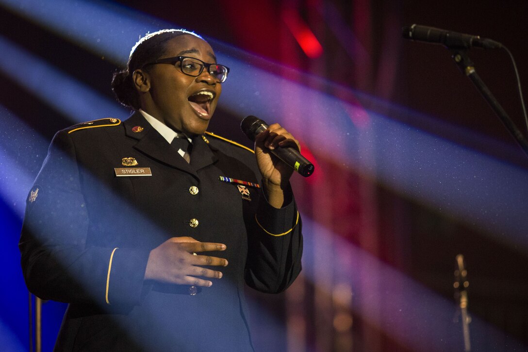 A soldier smiles while signing into a microphone with rays of blue light framing her.