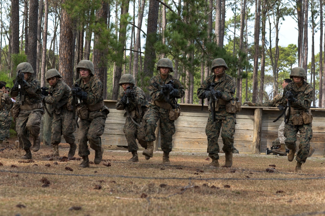 Marine Corps recruits tactfully step over barbed wire.