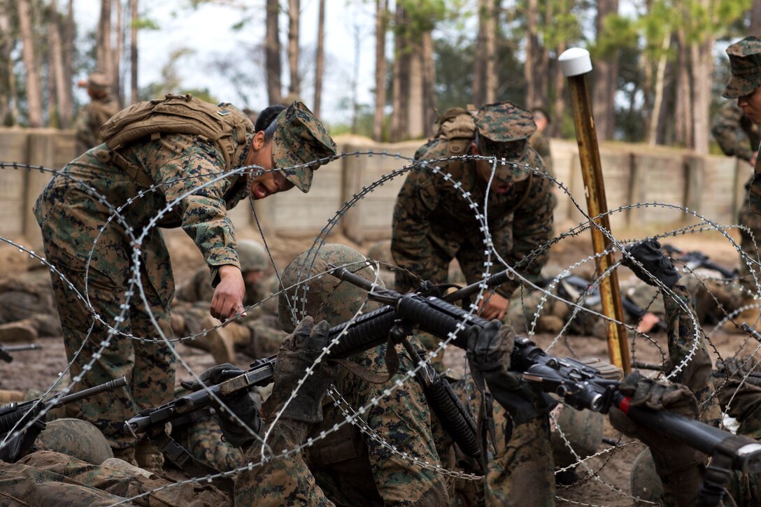 A Marine instructs recruits how to maneuver under concertina wire.