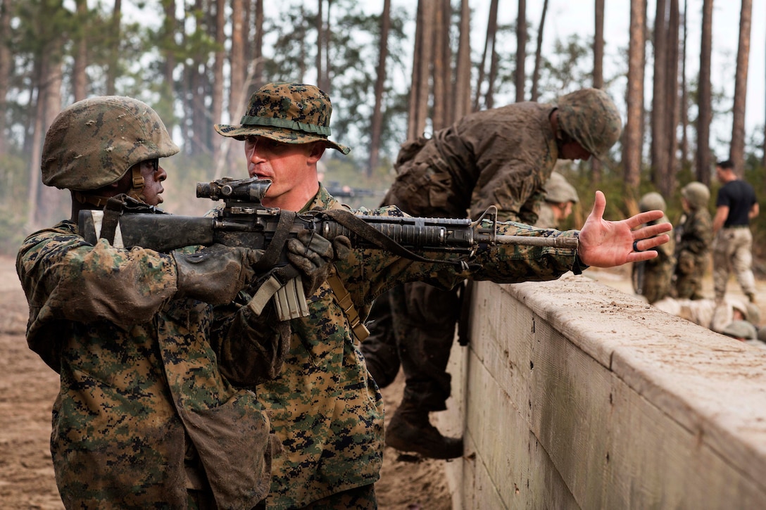 A Marine extends his harm while he stands next to another Marine holding a rifle.