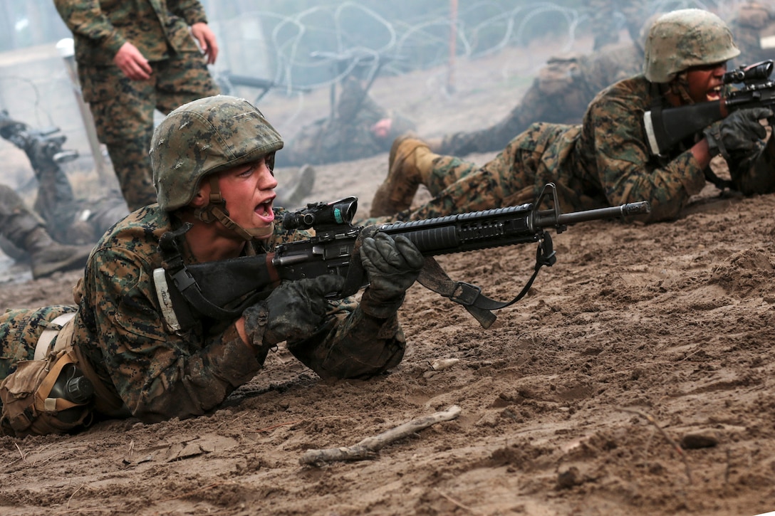 Marines aim rifles as they lie in the mud.