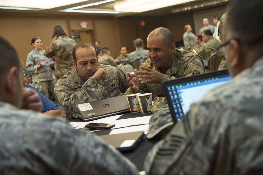 Military officials sit and talk around a table during a security workshop.