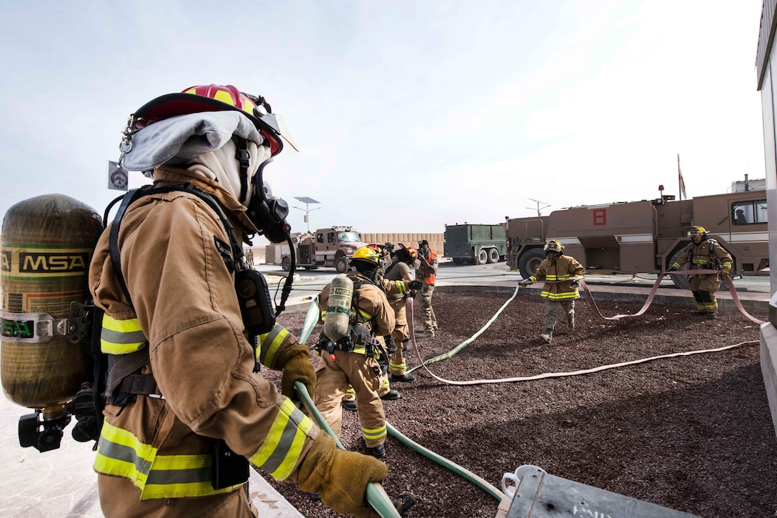 Air Force firefighters prepare their fire hoses before responding to a simulated structure fire during a coalition emergency response exercise.