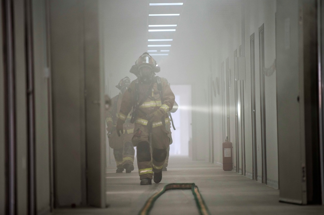 Air Force firefighters clear rooms in a smoke filled building responding to a simulated fire during a coalition emergency response exercise.