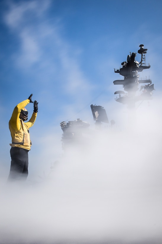 Navy Petty Officer 1st Class Edmond Scott signals to an aircraft on the flight deck of the aircraft carrier USS Theodore Roosevelt.