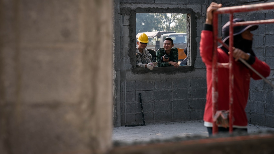 U.S. Army Spc. Bernard Fausto watches construction alongside his Royal Thai Army friend named "Dome" during construction of a school building at Nongphipadungkitwittaya School in Korat, Kingdom of Thailand, Feb. 7, 2018. Fausto is a horizontal engineer with 797th Engineering Company, 411th Engineer Battalion, and is a native of Tamuning, Guam. Humanitarian civic assistance projects conducted during the exercise support the needs and humanitarian interests of the Thai people. Cobra Gold 18 is an annual exercise conducted in the Kingdom of Thailand held from Feb. 13-23 with seven full participating nations.