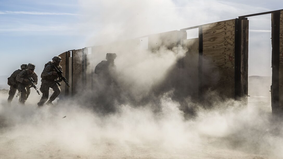 Marines participate in training to breach doors as smoke rises.