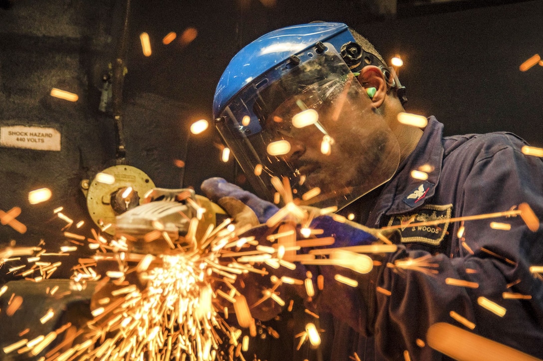 A sailor grinds a piece of metal in a ship's machine shop.