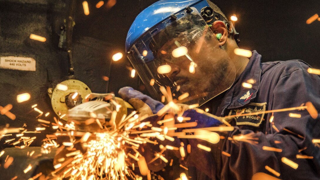 A sailor grinds a piece of metal in a ship's machine shop.