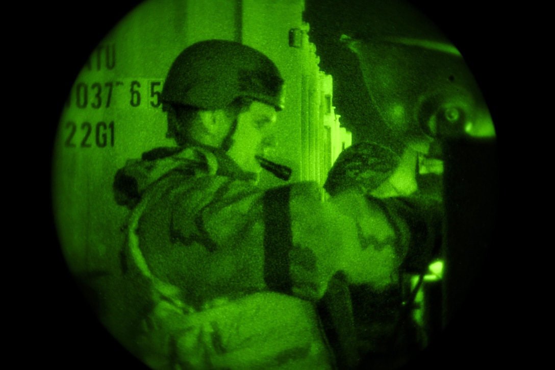 An airman holds a flashlight in his mouth during an exercise under a green light.