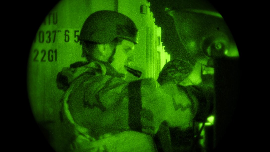 An airman holds a flashlight in his mouth during an exercise under a green light.