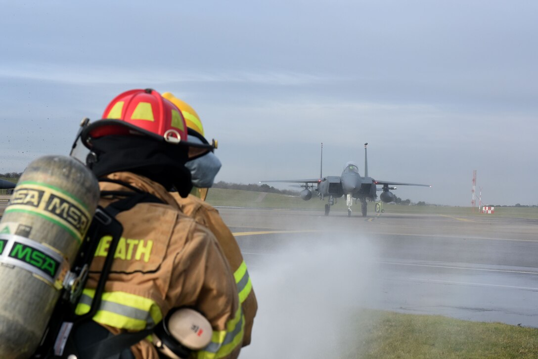 Airmen assigned to the 48th Civil Engineer Squadron train while at F-15E Strike Eagle taxis by at Royal Air Force Lakeneheath, England, Feb. 8. RAF Lakenheath firefighters are trained to respond to a wide variety of emergencies. (U.S. Air Force photo/Airman 1st Class Eli Chevalier)