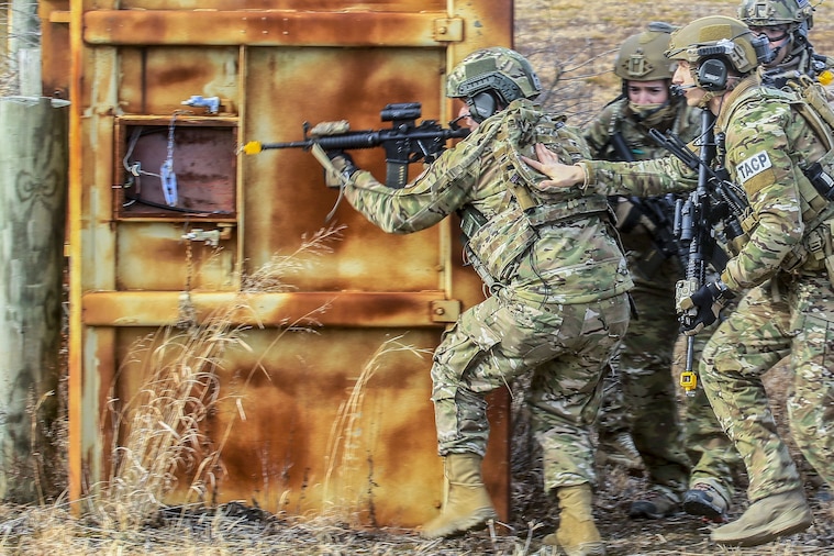 Four airmen move tactically to a target building.