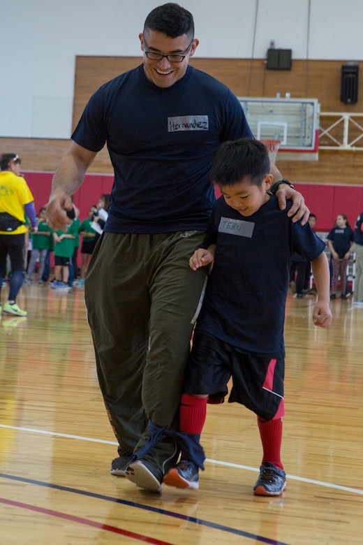 CAMP HANSEN, OKINAWA, JAPAN –  Pvt. Miguel A. Hernandez and a child from Nakagawa Elementary School work together during a three legged race during a Japan-U.S. Sports Exchange hosted by the Okinawa Defense Bureau Feb. 12 aboard Camp Hansen, Okinawa, Japan.