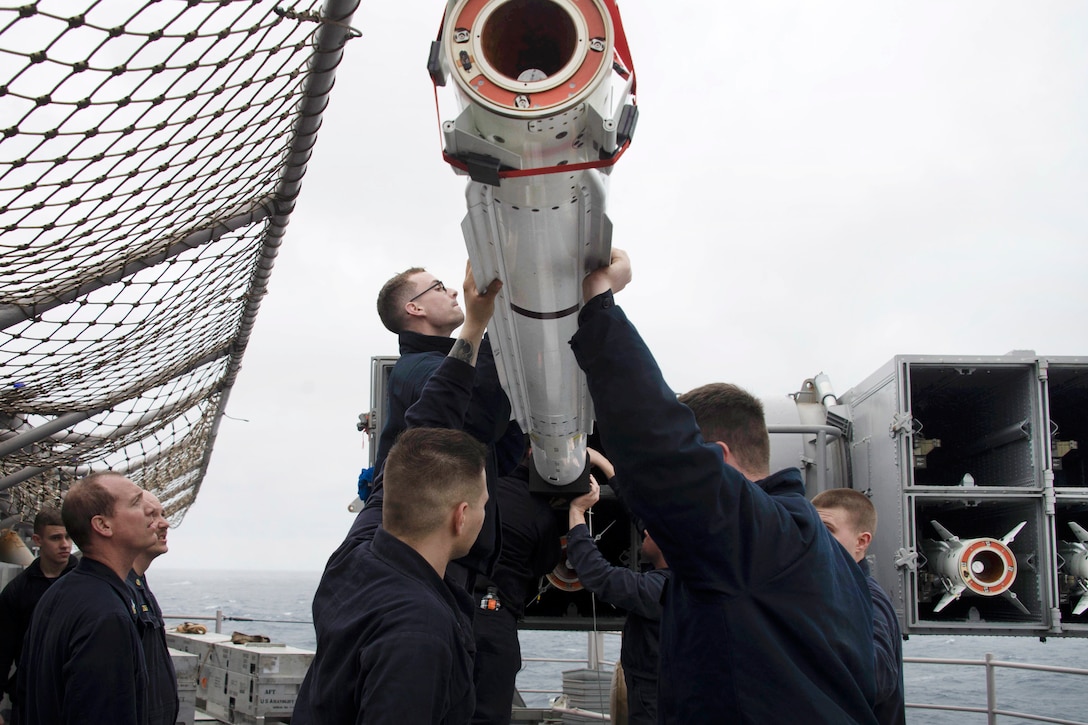Sailors load a missile into a NATO missile launcher on a ship.