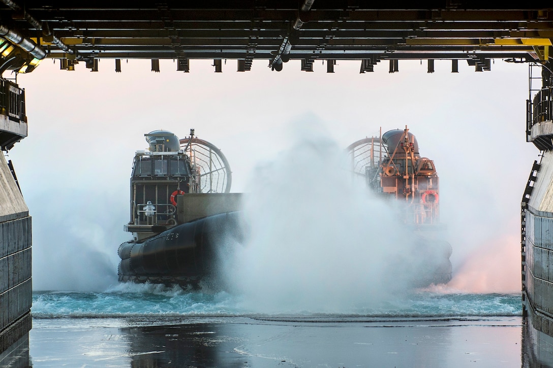 An air-cushioned landing craft splashes water as it enters a well deck.