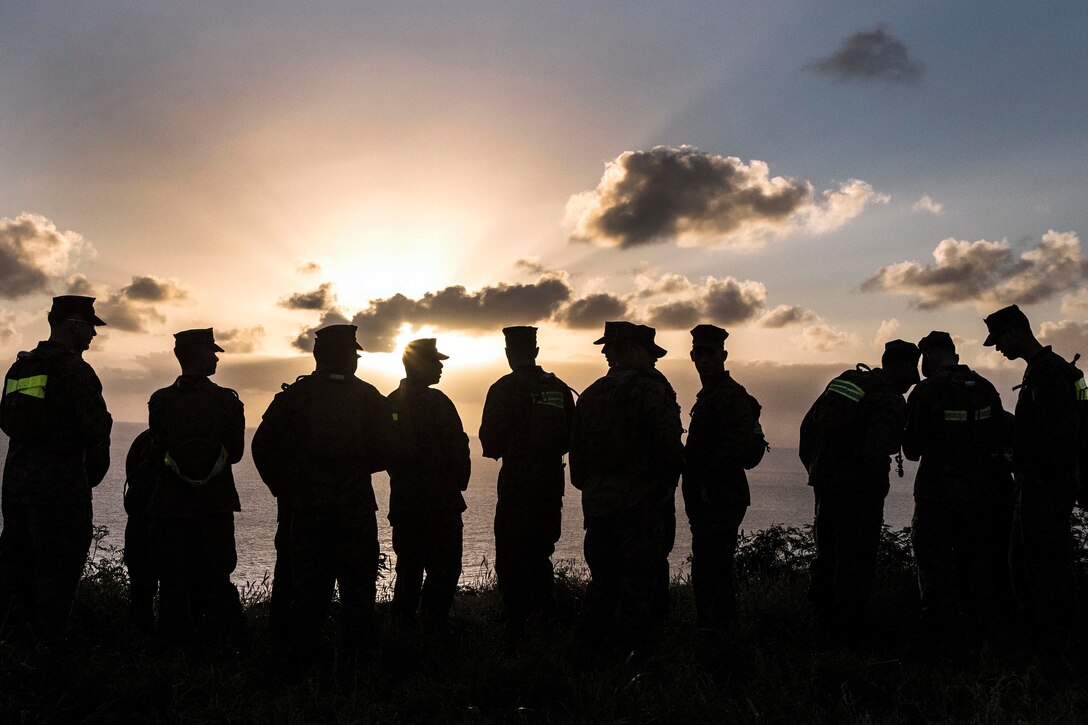 Silhouettes of Marines watching a sunrise over an ocean.