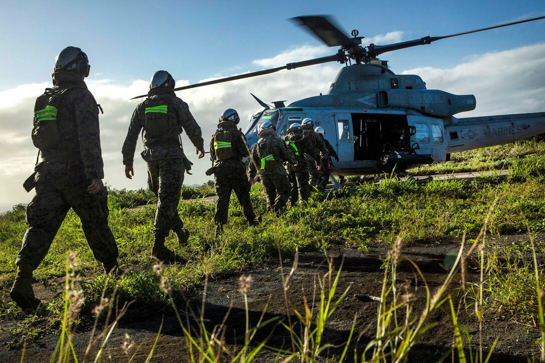 Marines walk in a line to board a UH-1N Huey helicopter.