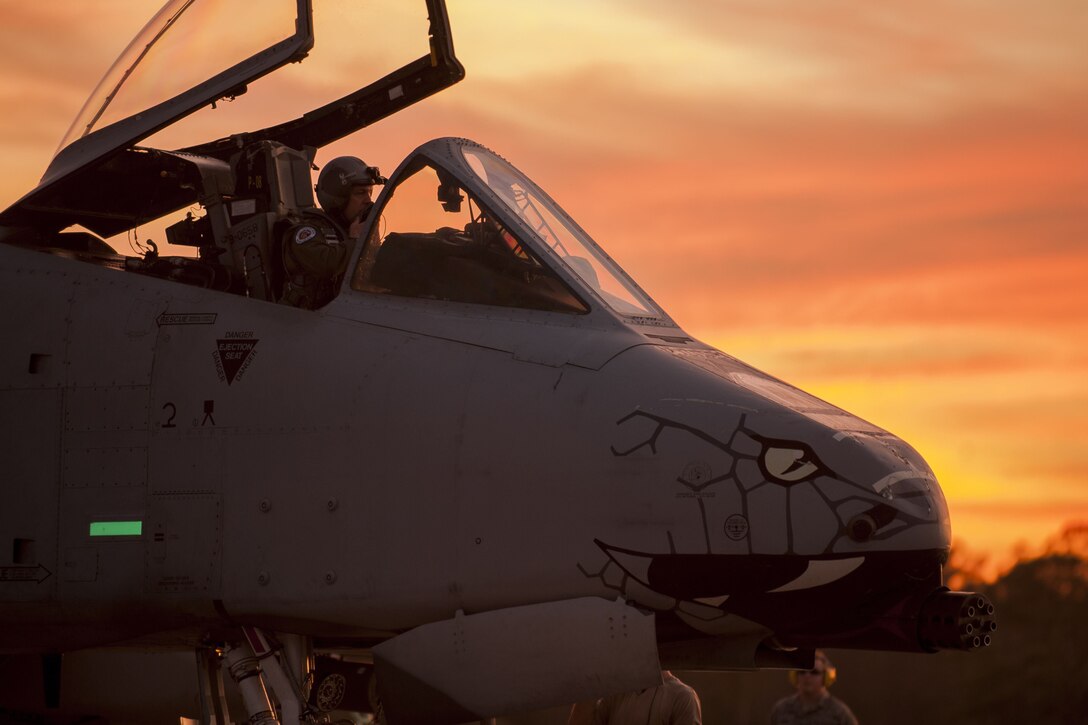 A pilot prepares a military aircraft for takeoff with an ornage sky in the background.