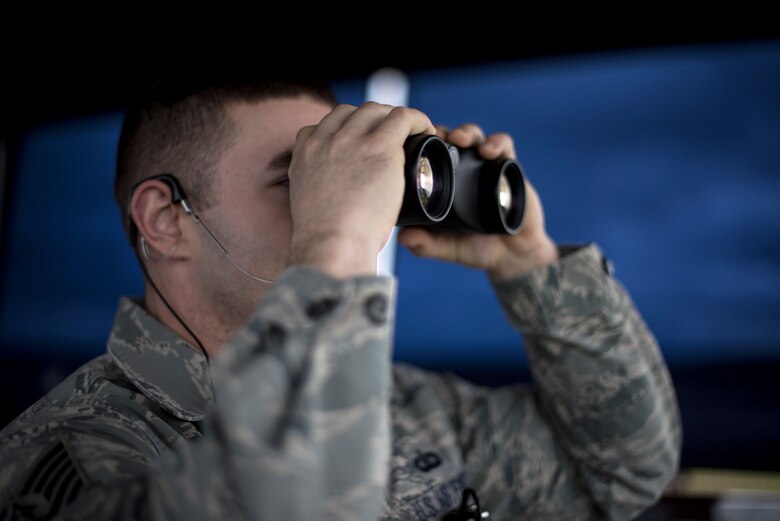 An Airman from the 48th Operations Support Squadron air traffic control tower peers through binoculars at Royal Air Force Lakenheath, England, Feb. 9, 2017. The tower sequences the arrival and departure of F-15s, helicopters and other airborne assets on and off the flightline. (U.S. Air Force photo/Senior Airman Malcolm Mayfield)