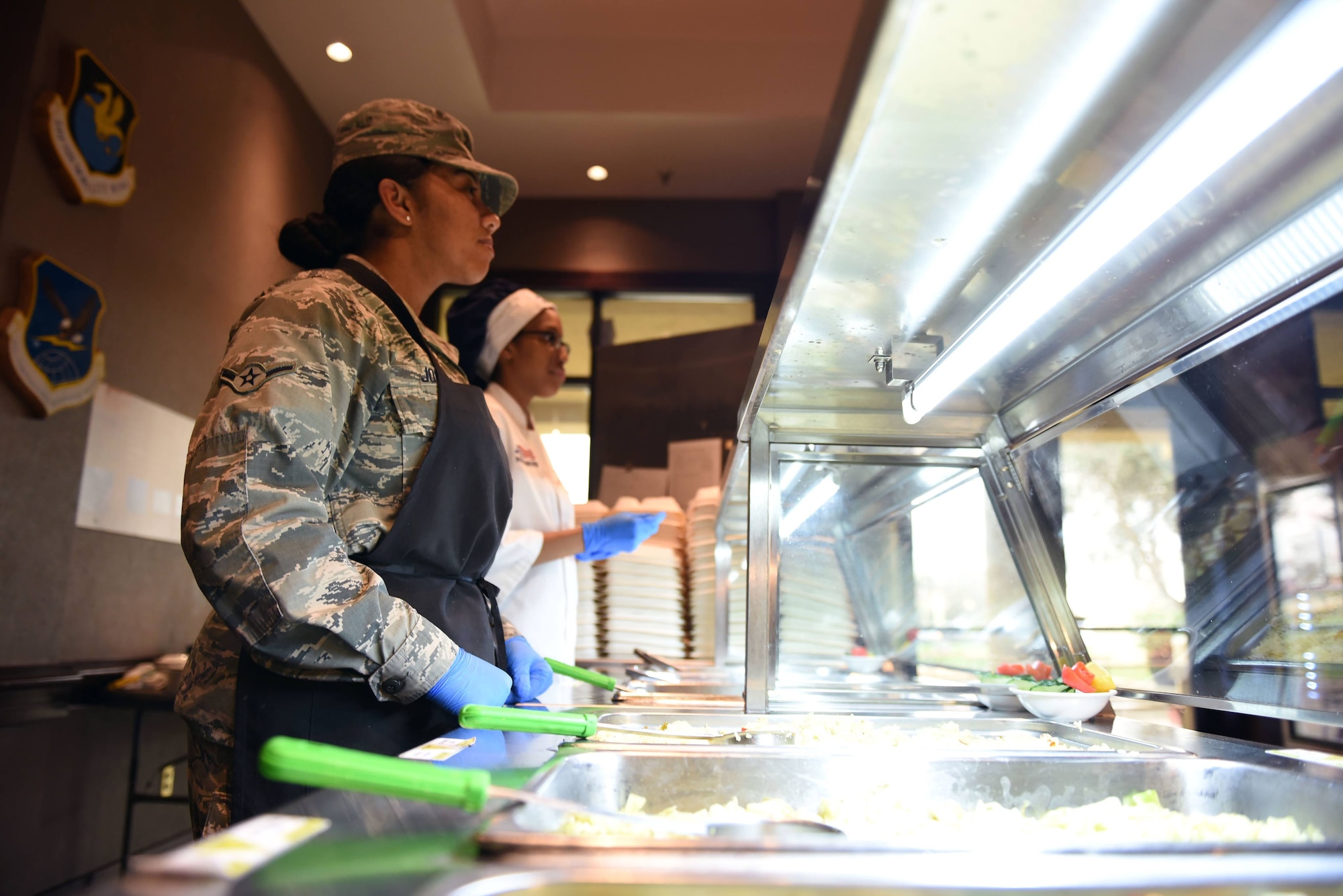 Airman Melanie Moore, 60th Force Support Squadron food service specialist, and Airman Domonique Jordan, 60th FSS food service apprentice, wait on customers at the base Dining Facility Feb. 11 at Travis Air Force Base, Calif. Moore and Jordan join the rest of the Sierra Inn DFAC team in representing Travis at the John L. Hennessy competition Feb. 20-23.