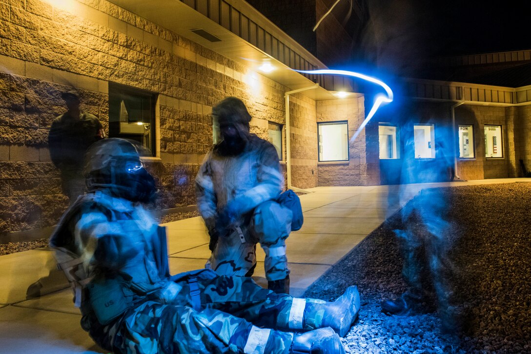 Airmen, illuminated in blue light, gather on a sidewalk outside a building.