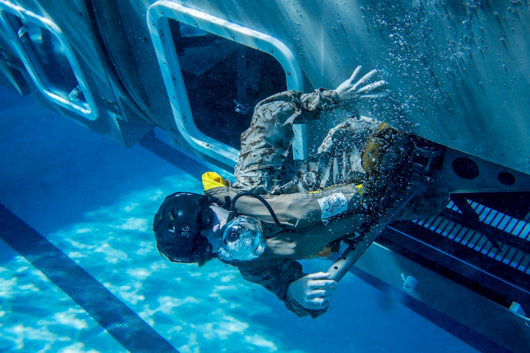 A Marine swims out from an opening in a mock helicopter at the bottom of a swimming pool.