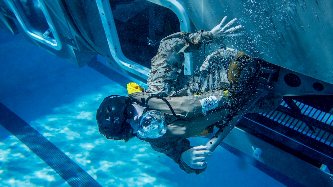 A Marine swims out from an opening in a mock helicopter at the bottom of a swimming pool.