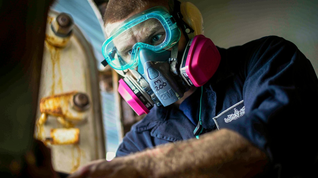 A sailor wearing goggles and a protective mask stares intently at something in front of him.