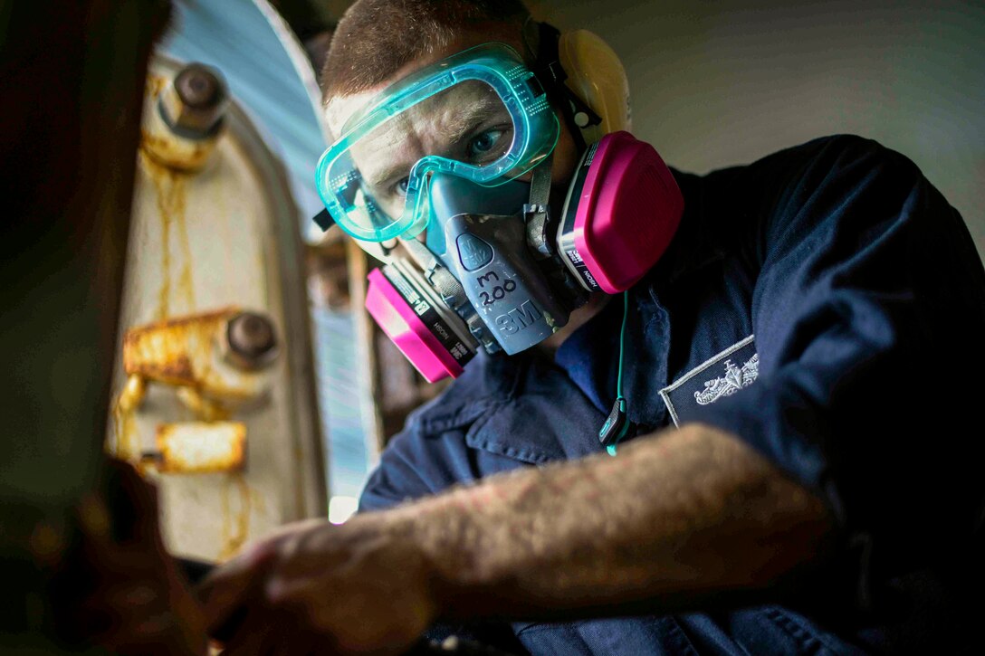 A sailor wearing goggles and a protective mask stares intently at something in front of him.