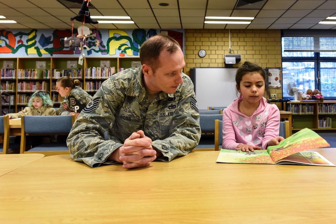 Two airmen listen as children read to them in a school library.
