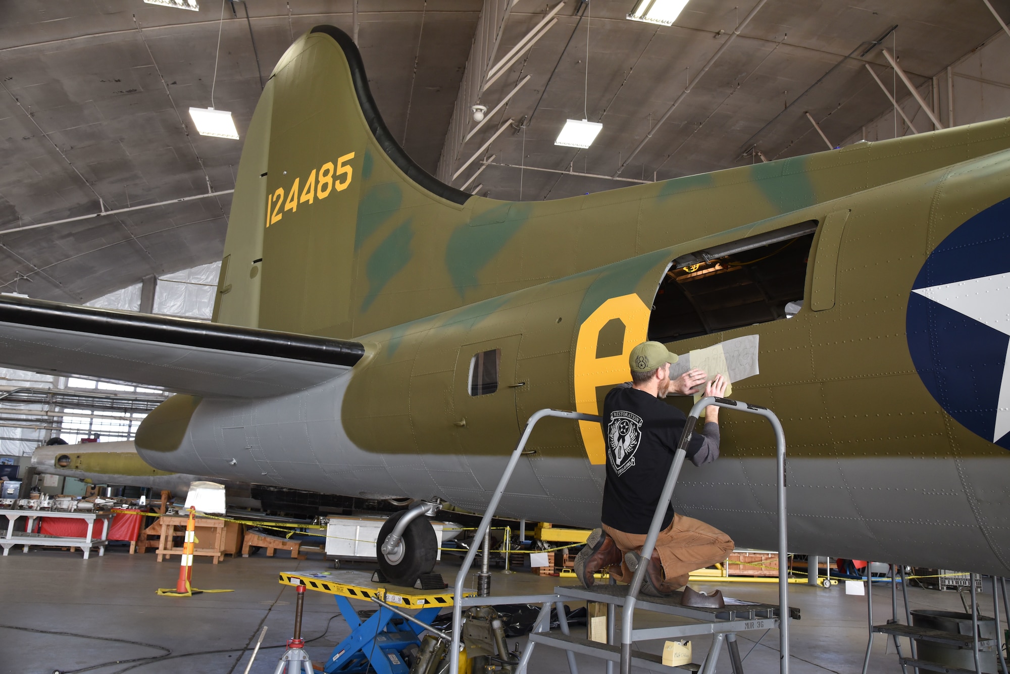 (01/25/2018) -- Museum restoration specialist Chad Vanhook paints the name 'Virginia' below the right waist gun position of the Boeing B-17F Memphis Belle as part of the aircraft restoration. (U.S. Air Force photo by Ken LaRock)