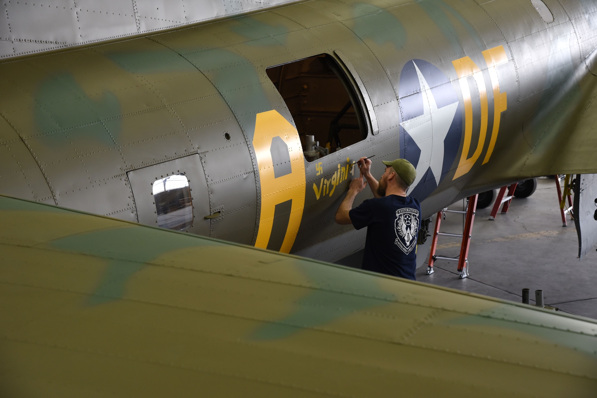 (01/25/2018) -- Museum restoration specialist Chad Vanhook paints the name 'Virginia' below the right waist gun position of the Boeing B-17F Memphis Belle as part of the aircraft restoration. (U.S. Air Force photo by Ken LaRock)