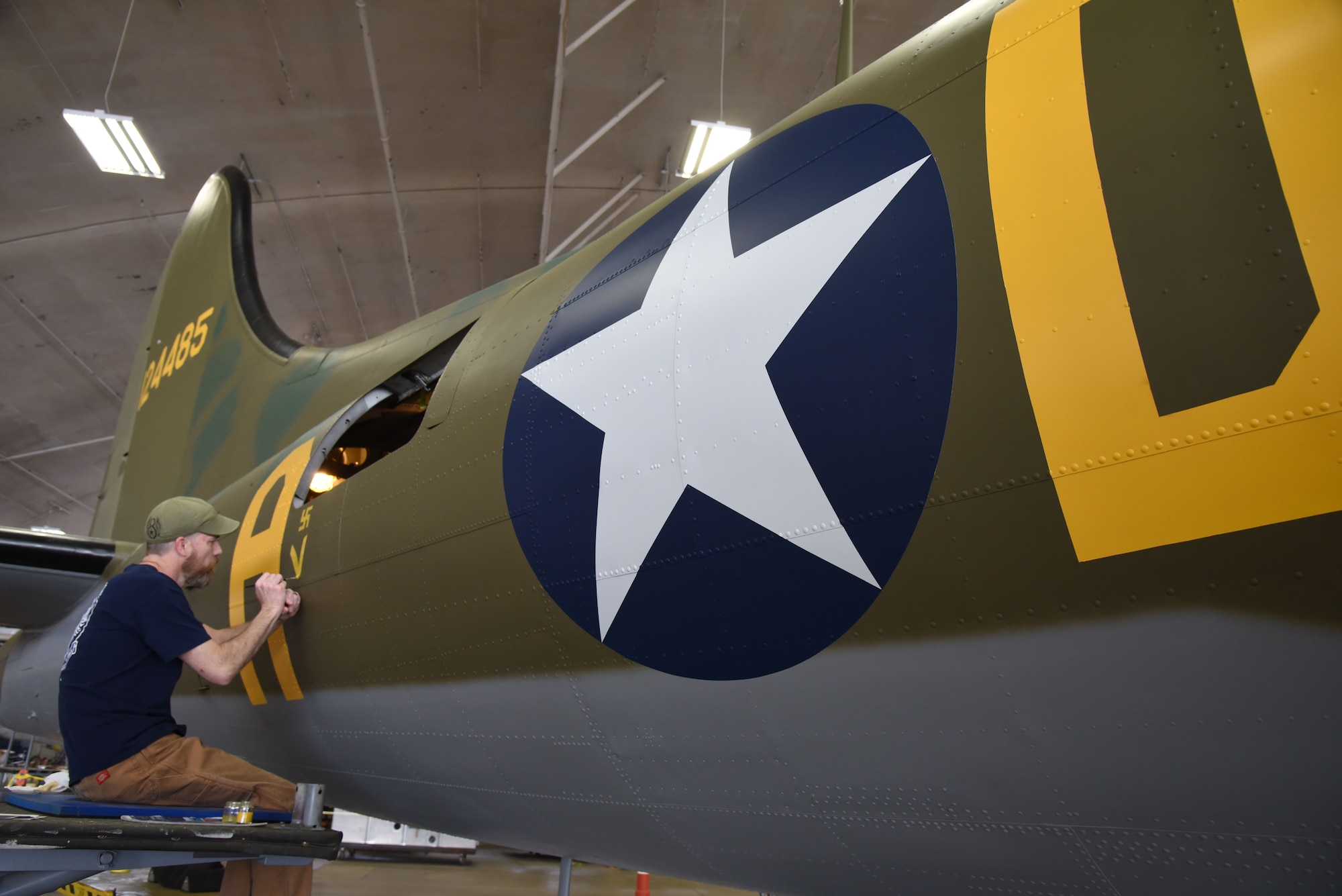 (01/25/2018) -- Museum restoration specialist Chad Vanhook paints the name 'Virginia' below the right waist gun position of the Boeing B-17F Memphis Belle as part of the aircraft restoration. (U.S. Air Force photo by Ken LaRock)