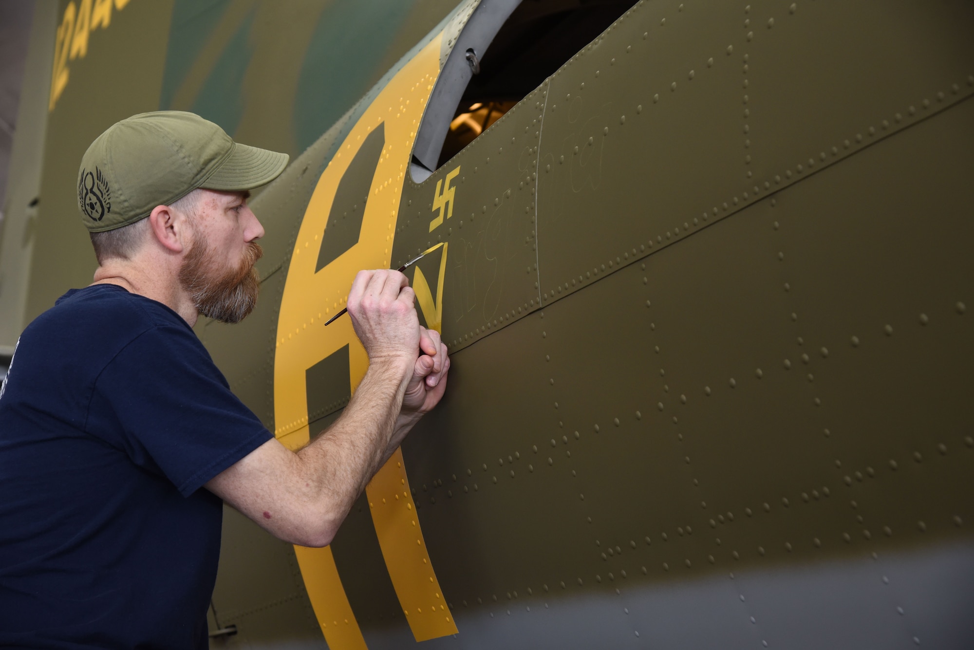 (01/25/2018) -- Museum restoration specialist Chad Vanhook paints the name 'Virginia' below the right waist gun position of the Boeing B-17F Memphis Belle as part of the aircraft restoration. (U.S. Air Force photo by Ken LaRock)