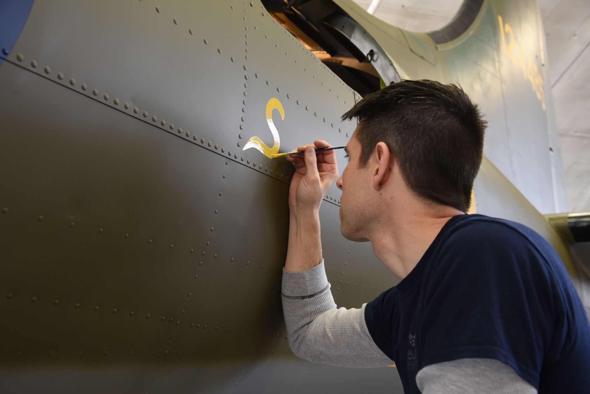 (01/25/2018) Museum restoration specialist Casey Simmons paints the letter 'S' for 'Sally' below the left waist gun position of the Boeing B-17F Memphis Belle as part of the aircraft restoration. Plans call for the aircraft to be placed on permanent public display in the WWII Gallery of the National Museum of the U.S. Air Force on May 17, 2018. (U.S. Air Force photo by Ken LaRock)