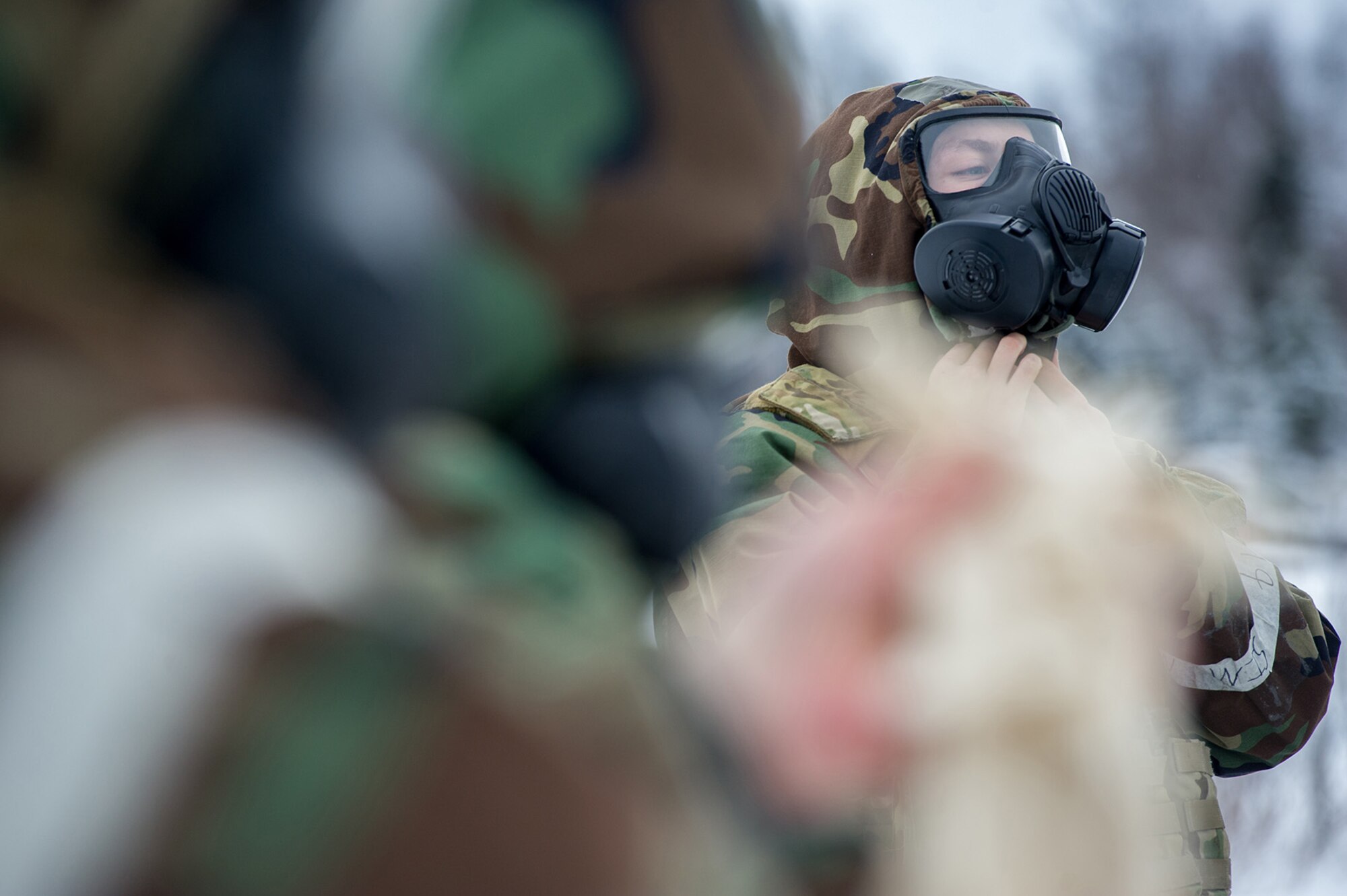 An Airman assigned to the 673d Civil Engineer Squadron, Explosives Ordinance Disposal Flight, adjusts the hood around his protective mask before a live-fire demolitions exercise in Mission Oriented Protective Posture 4 on Joint Base Elmendorf-Richardson, Alaska, Feb.14, 2018.  The Airmen were conducting EOD training in a simulated chemical weapons contaminated environment.