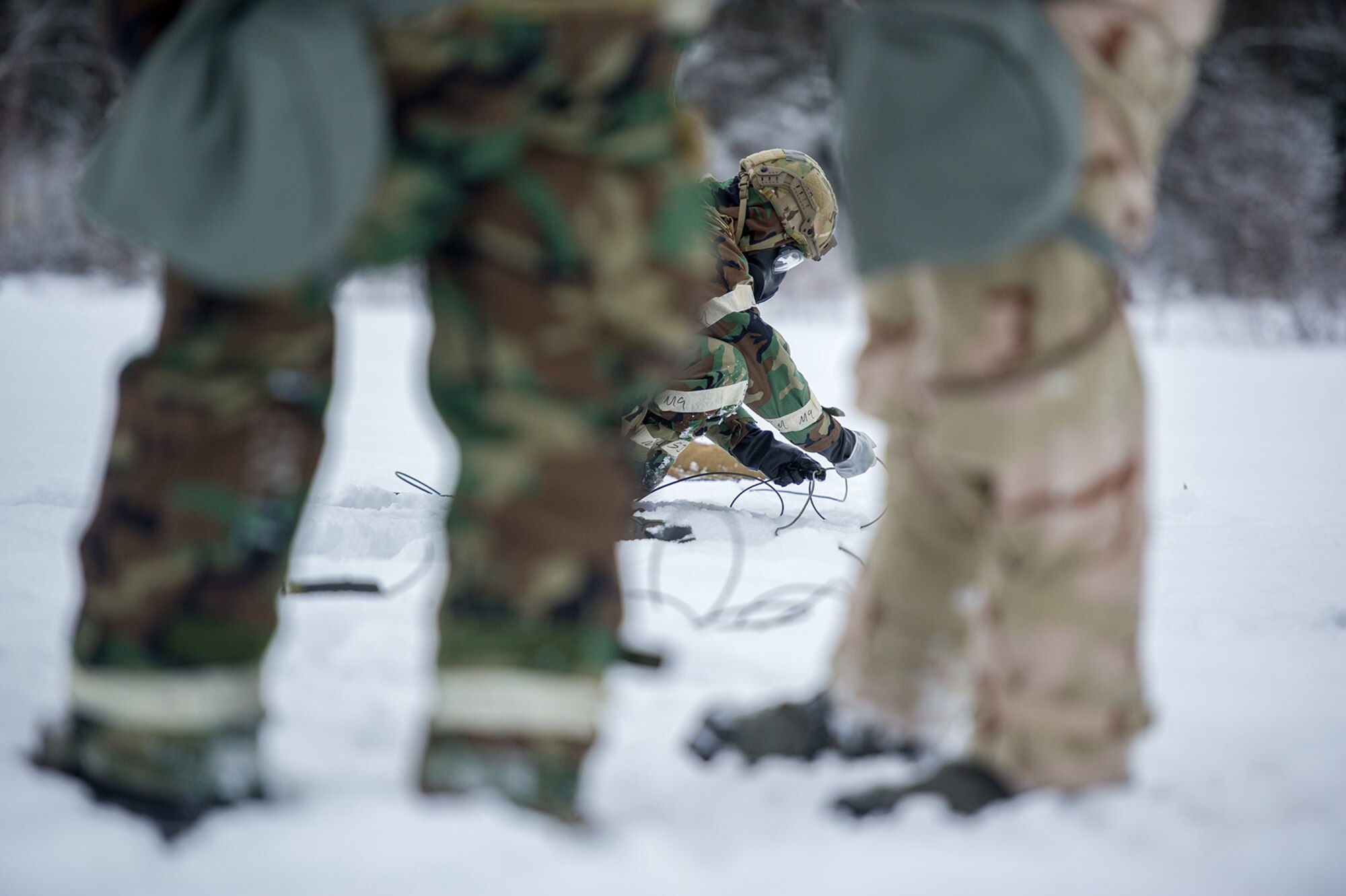 An Airmen assigned to the 673d Civil Engineer Squadron, Explosives Ordinance Disposal Flight, lays a charge in the snow before a live-fire demolitions exercise in Mission Oriented Protective Posture 4 on Joint Base Elmendorf-Richardson, Alaska, Feb.14, 2018.  The Airmen were conducting EOD training in a simulated chemical weapons contaminated environment.