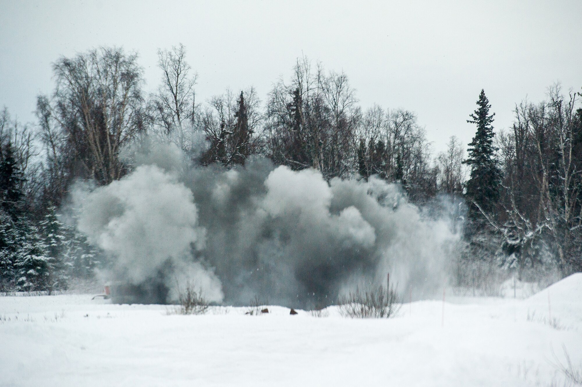 Explosive charges detonate throwing snow and debris into the air as Airmen assigned to the 673d Civil Engineer Squadron, Explosives Ordinance Disposal Flight, conduct a live-fire demolitions exercise in Mission Oriented Protective Posture 4 on Joint Base Elmendorf-Richardson, Alaska, Feb.14, 2018.  The Airmen were conducting EOD training in a simulated chemical weapons contaminated environment.