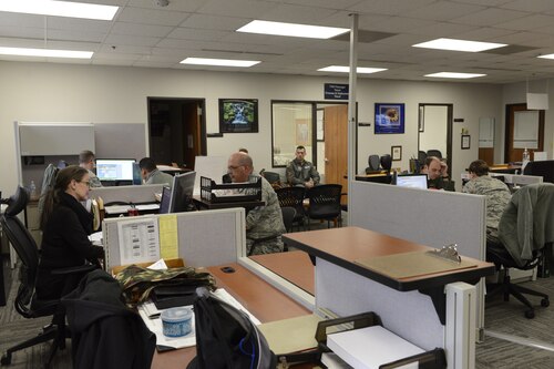 A large office is filled with desks and people working at those desks.