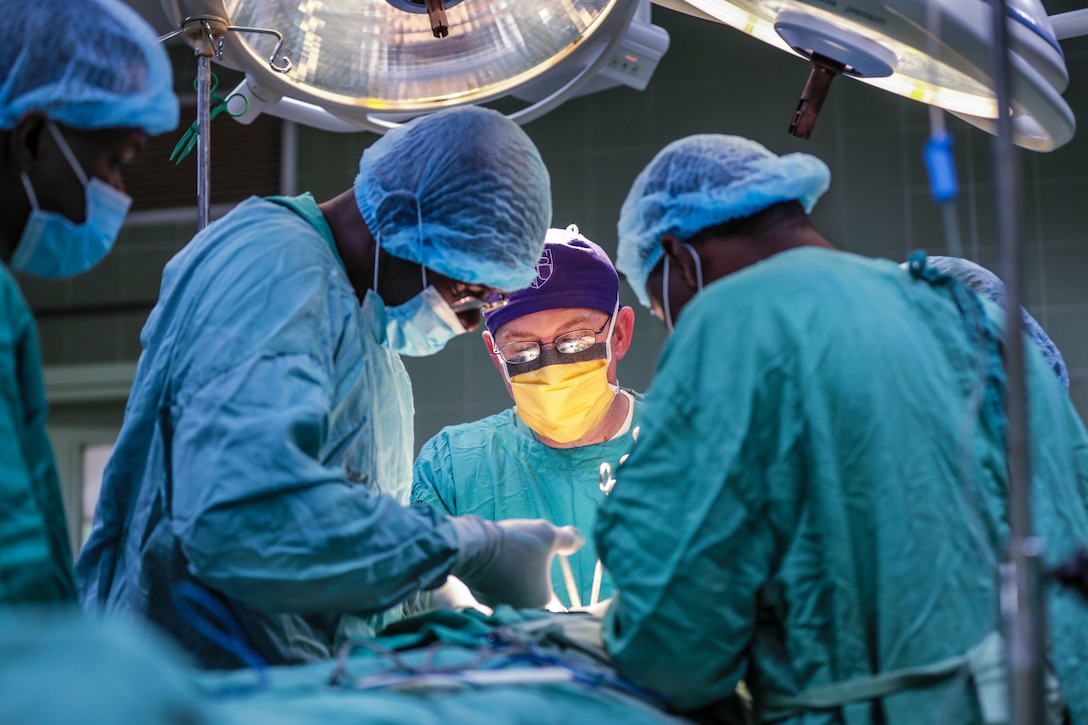 Medical personnel in blue gowns perform surgery at a hospital.